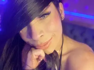 MacaSweet poses with her long dark hair falling over her face, showing her eyes and smile in a close-up shot.