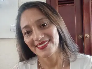 MaciaMuller smiling at the camera with long brown hair and red lipstick, wearing a white top.