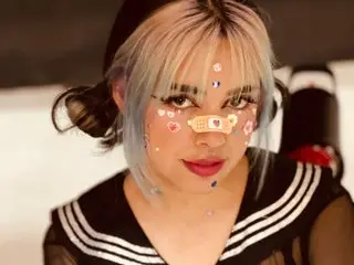 MaddieWaves shows off her light blue hair and face, wearing a black and white striped top while looking directly at the camera.