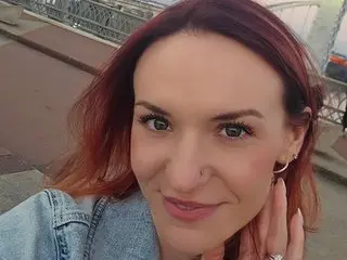 MadelynSpark smiles while looking at the camera, showing her long reddish hair and a close-up view of her face and shoulders.