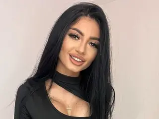 MadisonVixen poses with long black hair and a direct gaze, wearing a black long-sleeved top against a plain light background.