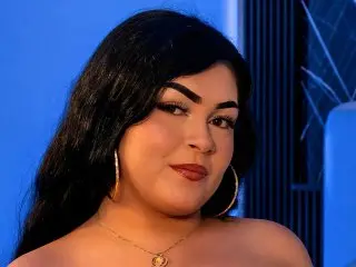 MadissonJoe poses with a soft smile, showing her dark hair and face against a blue background.