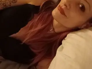 MagdalenaIvey lying back with her long pink hair spread out, wearing a black top and showing her face and neck.