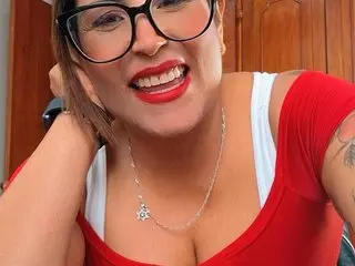 MajoSoussa smiles while wearing black glasses and a red top, showing her teeth and hair pulled back.