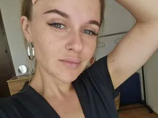 MaribelRiverr looks directly at the camera with her hand behind her head, showing her light brown hair and nose ring in a close-up shot.