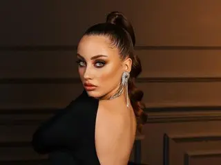 MaribelleVinnie poses with her hair in a high ponytail, wearing a black top and silver earrings against a dark background.
