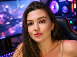 Marivelle poses with a direct gaze, showing her long brown hair and bare shoulders in a dimly lit room with purple neon lighting.
