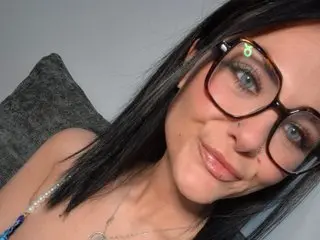 MarriedMiaUK smiles while posing with her long black hair down, wearing large glasses in a close-up shot.