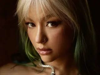 MaryMilan poses with her blonde hair framing her face, wearing a silver necklace and looking directly at the camera.