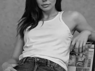 Young woman in a white tank top and denim jeans sitting relaxed with a newspaper in a black and white portrait.