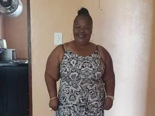 Mature_Milfxxx poses facing the camera wearing a black and white patterned sundress, showing her shoulders and hair tied up in a bun.