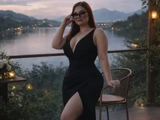 Curvy woman in a black evening dress posing on a scenic balcony overlooking a lake at sunset.