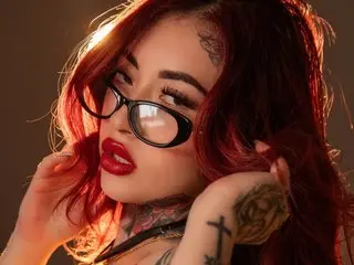 MeganMontiel poses with her red hair framing her face, showing her dark eyes, red lips, and neck tattoos.