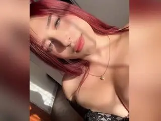 Megan_rowland poses with long red hair, wearing a black patterned bra that shows off her cleavage and chest.
