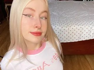 MelaniePlay poses close-up with long blonde hair, wearing a white t-shirt with pink trim, looking directly at the camera.