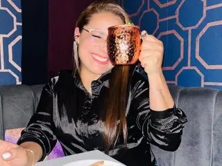 Meli_pretty smiles while sitting on a couch and holding a copper mug to her lips.
