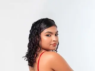 MelodyAlvarez looks over her shoulder with wavy dark hair against a plain white background.