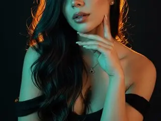 MelodyCarson poses with long dark hair and a black top against a dark background.