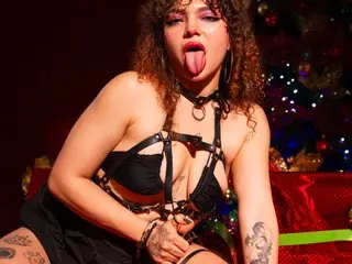 MentalLagoon poses with her tongue out, wearing a black strappy harness bra and black bottoms, showing her chest and hair.
