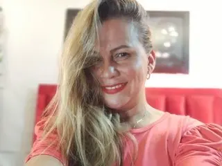 MeryJeeans smiles while posing in a pink top, showing her long blonde hair and light skin in a close-up shot.