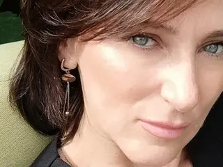Close-up portrait of a woman with light eyes and brown hair wearing elegant drop earrings in soft natural light.