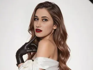 Mia_Crush poses with a hand to her chin, wearing a white off-the-shoulder top and red lipstick against a white background.