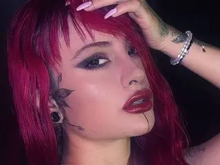 Miaa_Stonee shows off her red hair and dark eye makeup in a close-up headshot against a black background.