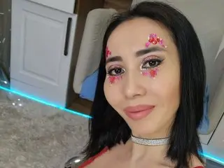 Miachoo, a woman with long black hair, looks at the camera wearing a silver choker and a red top.