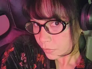 MiawMiawMiaw looks into the camera with dark hair and glasses, wearing a black floral top while sitting in a dark car seat.