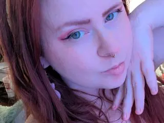 Close-up portrait of a young woman with red hair and pink eye makeup in soft, dreamy lighting.