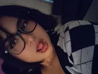 MidnigthSg looks at the camera with a pouty mouth and glasses, wearing a black and white patterned top.