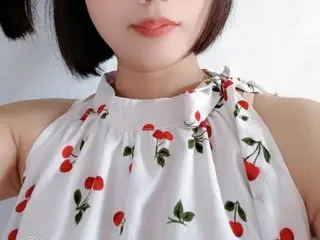 MieBae wears a white sleeveless top with a red cherry print, showing her neck and shoulders against a plain white background.