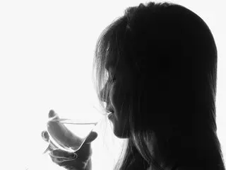 Silhouette of a woman drinking from a glass against a bright white background in a moody black and white style.