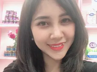 Smiling young woman with dark hair in a retail shop setting surrounded by beauty products.