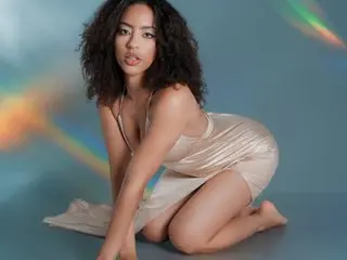 Young woman in a champagne silk slip dress sitting against a dreamy blue background with rainbow light flares.