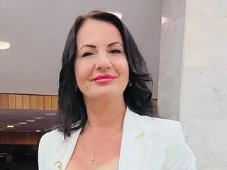 Misjokiya has long dark hair and is wearing a white blazer, looking directly at the camera with a smile.