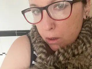 MissAlicex wearing red glasses and a brown furry scarf, looking directly at the camera with a neutral expression.