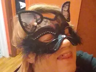 MissKittyFox4u wears a black lace mask over her eyes and smiles, showing her teeth against a plain background.