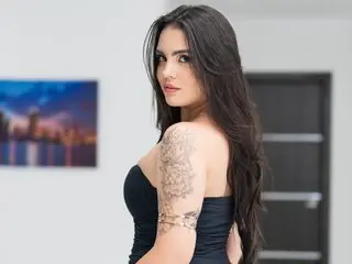 MissValeriie poses with her long dark hair down, showing off her shoulder and arm tattoos while wearing a black top.