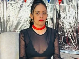 Miss_Nicolle wears a sheer black long-sleeve top and a red choker while posing in front of a silver foil background.