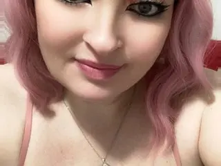 Miss_perdu, a woman with pink hair, looks at the camera while wearing a thin pink strap and a silver necklace.
