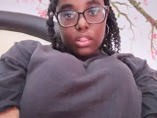 Misscc99 looks directly at the camera wearing a black t-shirt with her dark curly hair framing her face.