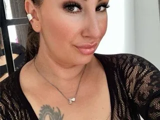 Misscorpion69 looks into the camera with a slight smile, wearing a black lace top and a delicate silver necklace.