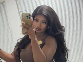 Misskjay poses for a mirror selfie, showing her long dark hair and brown top while holding her phone.