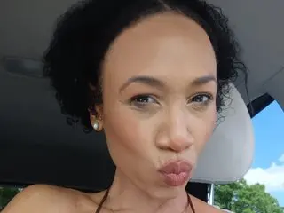MistressJacksonMonroe pouts her lips while looking directly at the camera, showing her dark curly hair and bare shoulders.