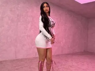 Young woman in a white mini dress and pink lace-up boots posing in a pink studio setting.