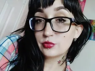 MistressTatianaBelen has long black hair and glasses, wearing a plaid shirt and red lipstick while looking at the camera.