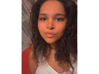 Mistress_Sasha looks directly at the camera with a neutral expression, showing her face and curly dark hair against a plain background.