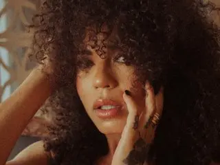 Mo_Rafaella poses with her hands near her face, showing her thick, curly hair and dark eyes.