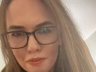 Molly_Brook wearing glasses and looking into the camera with her long blonde hair.